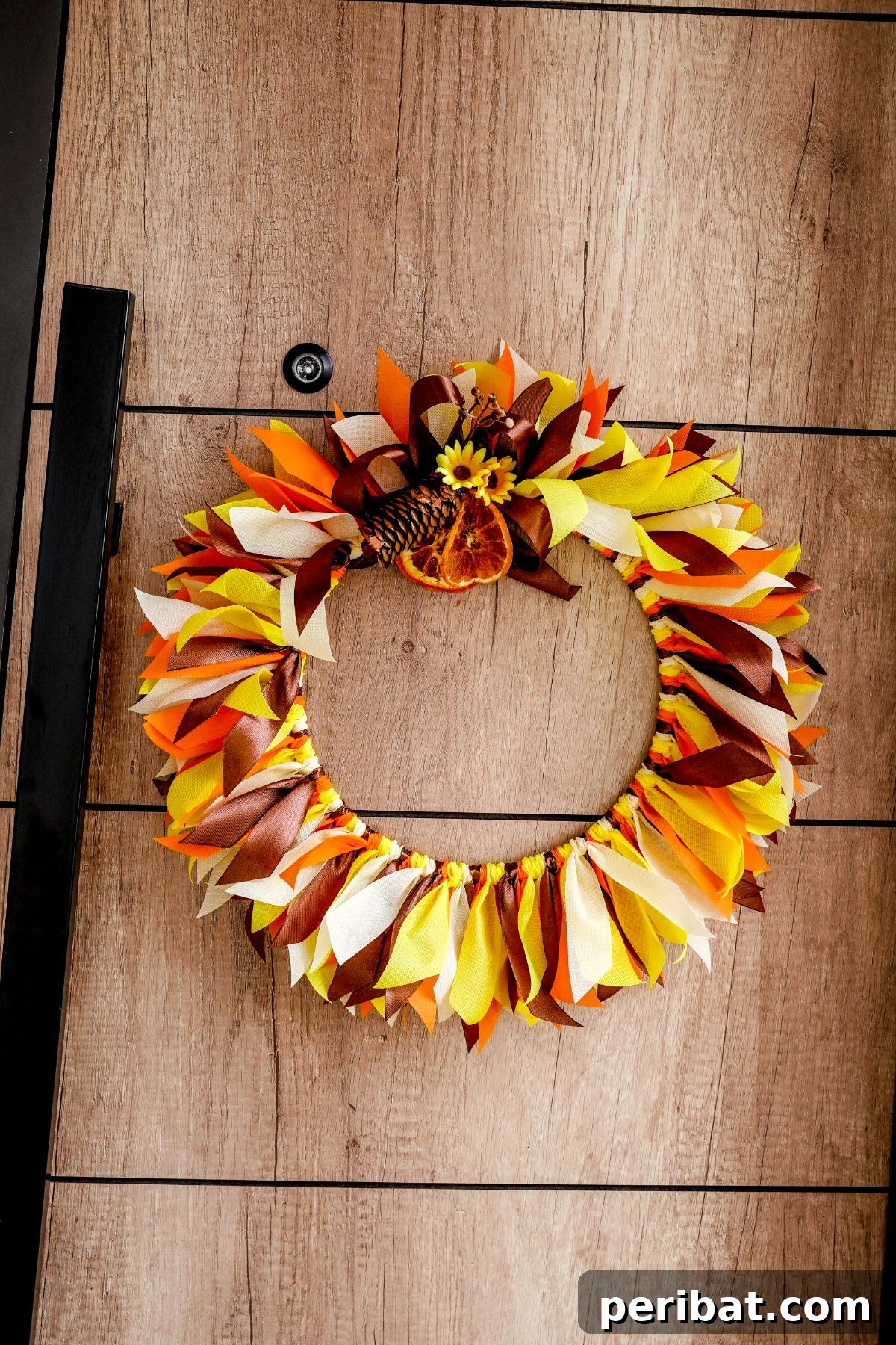 Autumn Farmhouse Wreath from Upcycled Fabric Scraps 17 A charming fall rag wreath hanging on rustic wood paneling, showcasing cozy autumn decor.