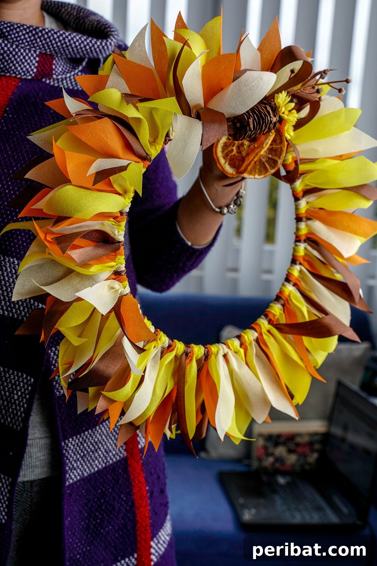 Autumn Farmhouse Wreath from Upcycled Fabric Scraps 19 A woman in a purple sweater proudly holding her finished fall rag wreath, ready for display.