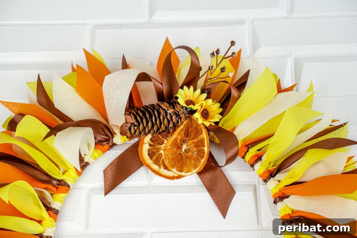 Autumn Farmhouse Wreath from Upcycled Fabric Scraps 3 Close-up of a decorative bow on an autumn wreath, adorned with dried orange slices and artificial flowers.