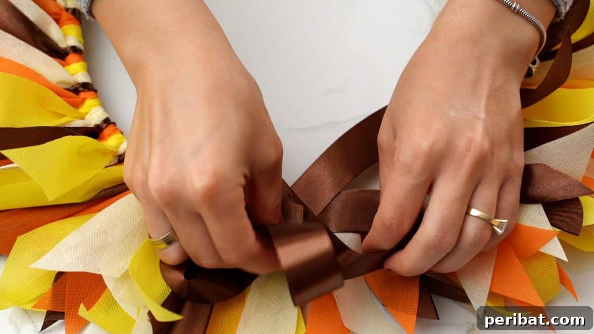 Autumn Farmhouse Wreath from Upcycled Fabric Scraps 22 A hot glue gun is being used to carefully secure a rustic brown bow onto the top of a fall rag wreath.