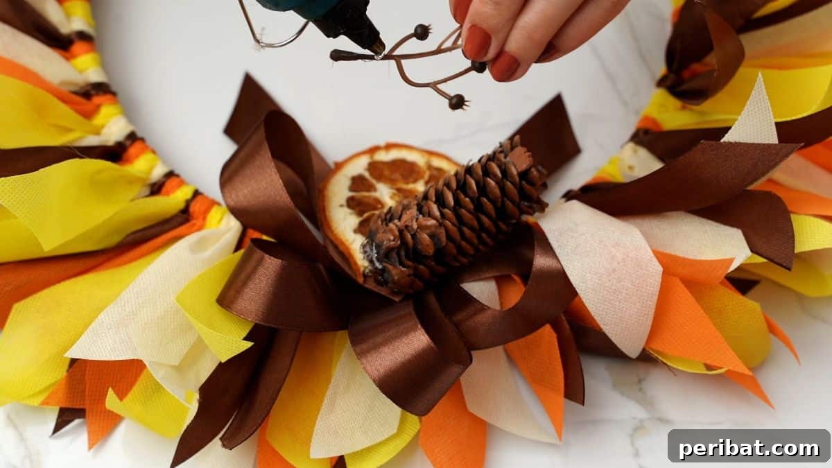 Autumn Farmhouse Wreath from Upcycled Fabric Scraps 23 Small, natural pinecones are being meticulously glued onto the autumn-themed rag wreath to enhance its rustic charm.