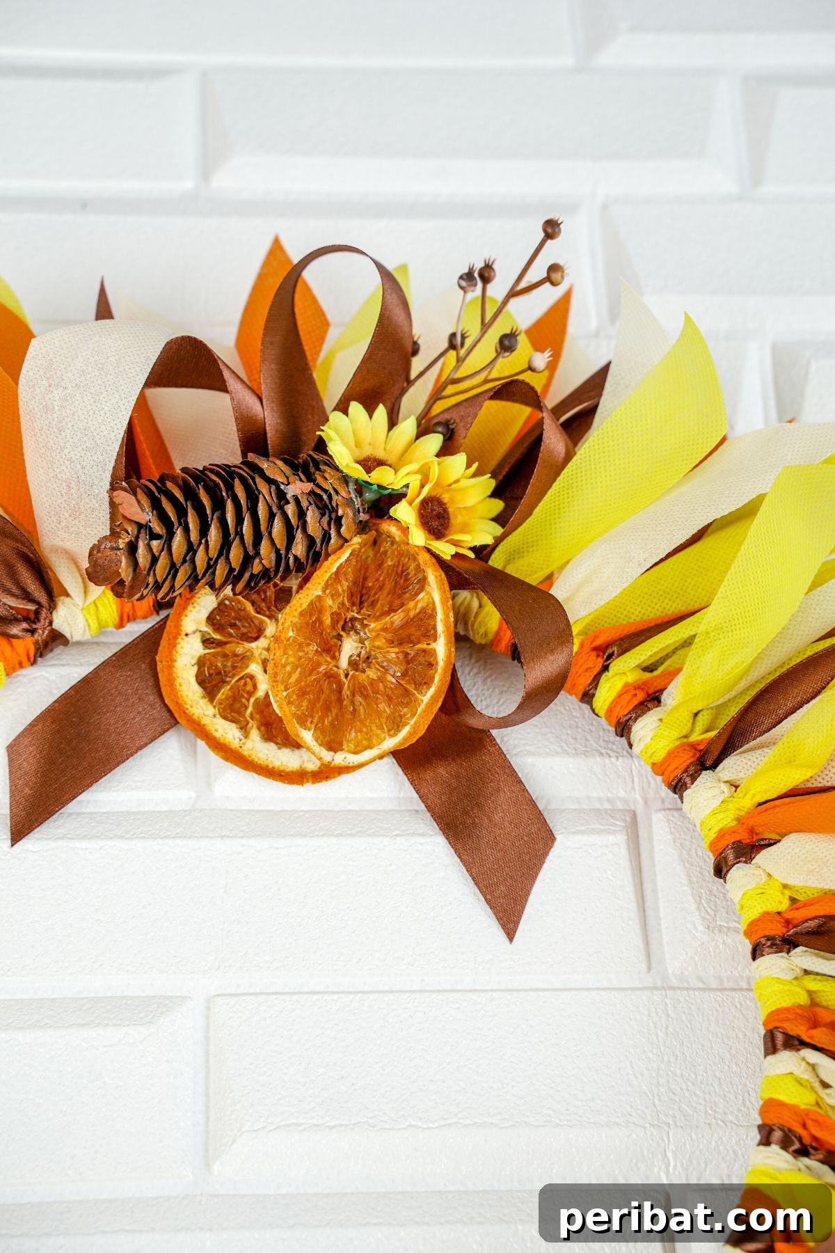 Autumn Farmhouse Wreath from Upcycled Fabric Scraps 24 A finished fall rag wreath adorned with dried orange slices and pinecones, ready for hanging, against a blurred background.