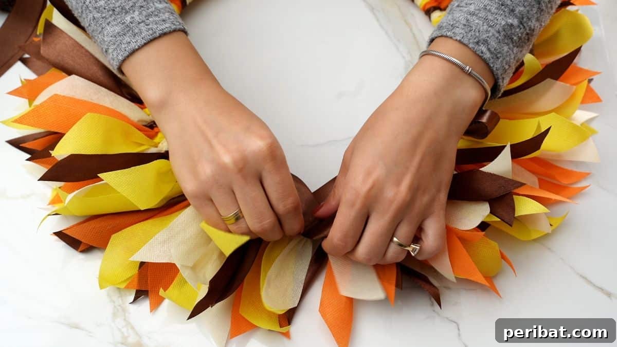Autumn Farmhouse Wreath from Upcycled Fabric Scraps 10 A rustic brown bow being carefully glued onto a partially completed fall rag wreath, ready for further embellishment.