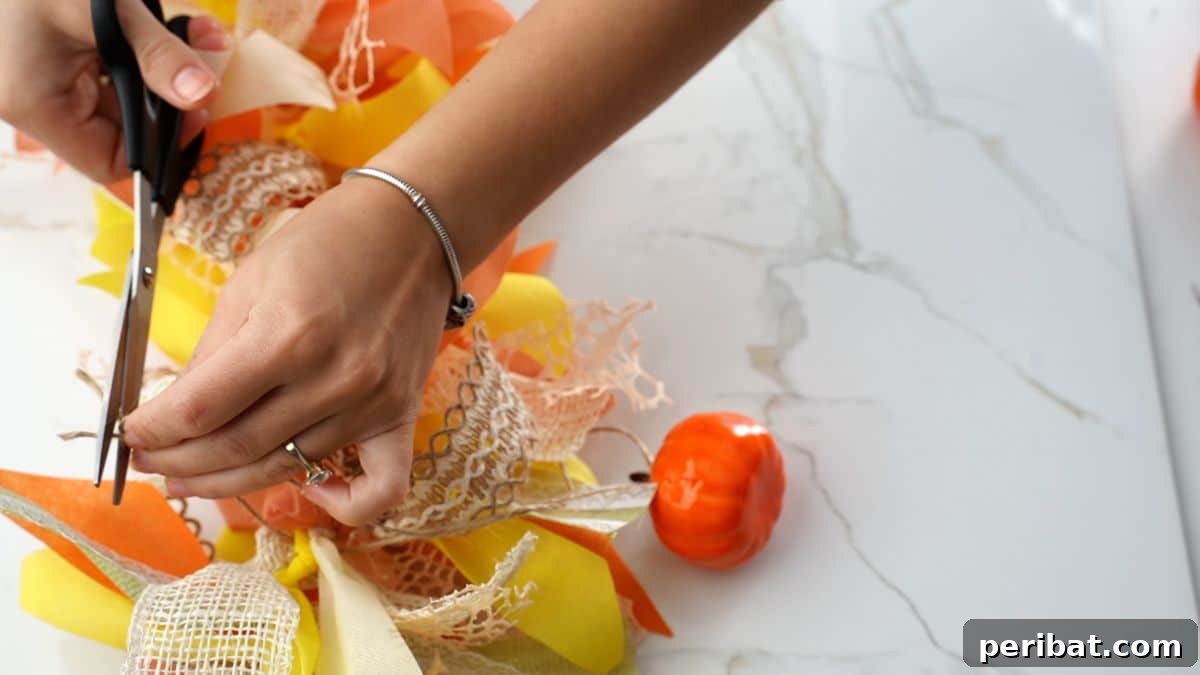 Close-up of scissors cutting excess twine from a completed fall rag garland with pumpkin
