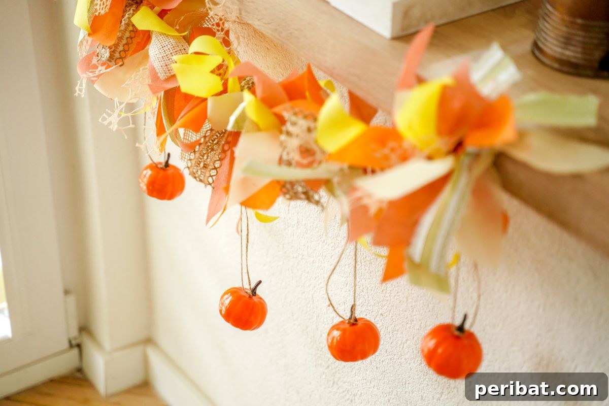 Close-up of a fall rag garland with mini pumpkins and rustic fabric strips, against a white wall