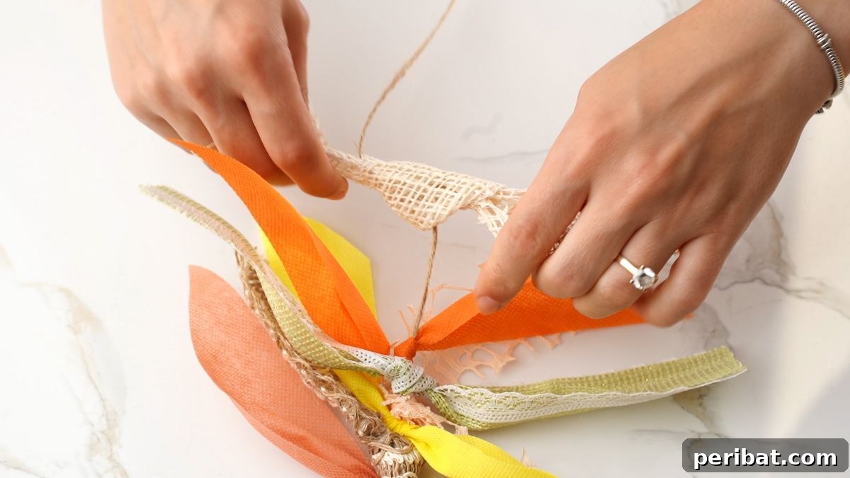 Close-up of hands tying a wider strip of burlap fabric onto a twine garland base