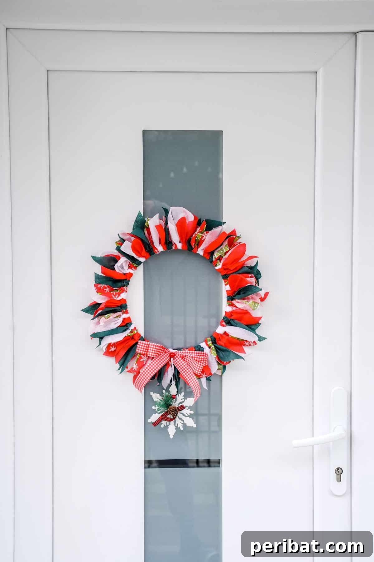 Effortless Festive Fabric Wreath 2 White door with a rustic wooden frame holding a vibrant Christmas rag wreath featuring red, green, and white fabrics.