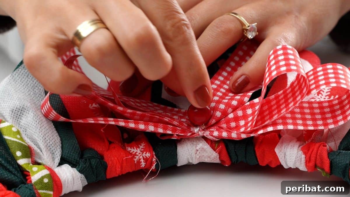 Effortless Festive Fabric Wreath 11 A hand applying hot glue to secure a small decorative bead on top of a festive bow, which is affixed to the completed Christmas rag wreath.