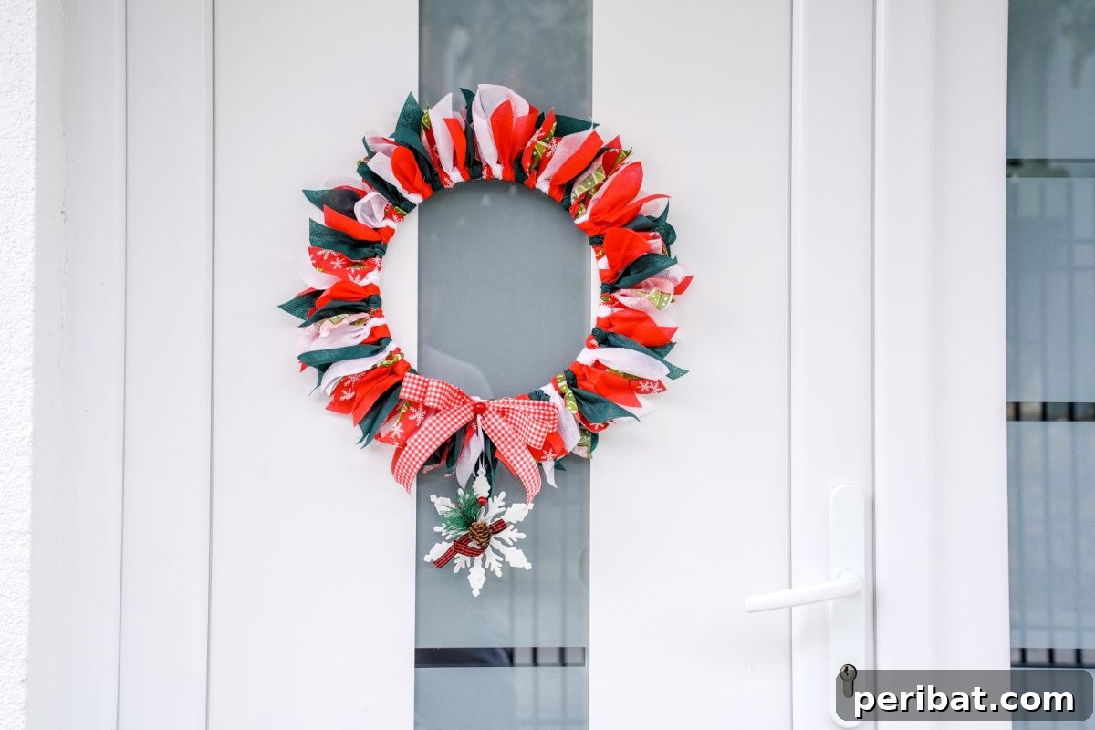 Effortless Festive Fabric Wreath 16 A festive Christmas rag wreath, featuring a delicate white snowflake hanging from its bottom, elegantly displayed on a clean white door, ready to welcome guests.