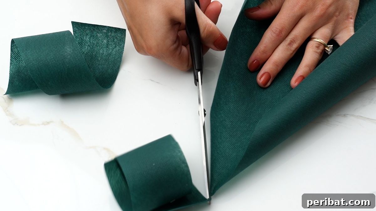 Effortless Festive Fabric Wreath 6 A hand holding scissors, demonstrating the cutting of multiple green fabric strips, ensuring consistent length and width for the wreath.