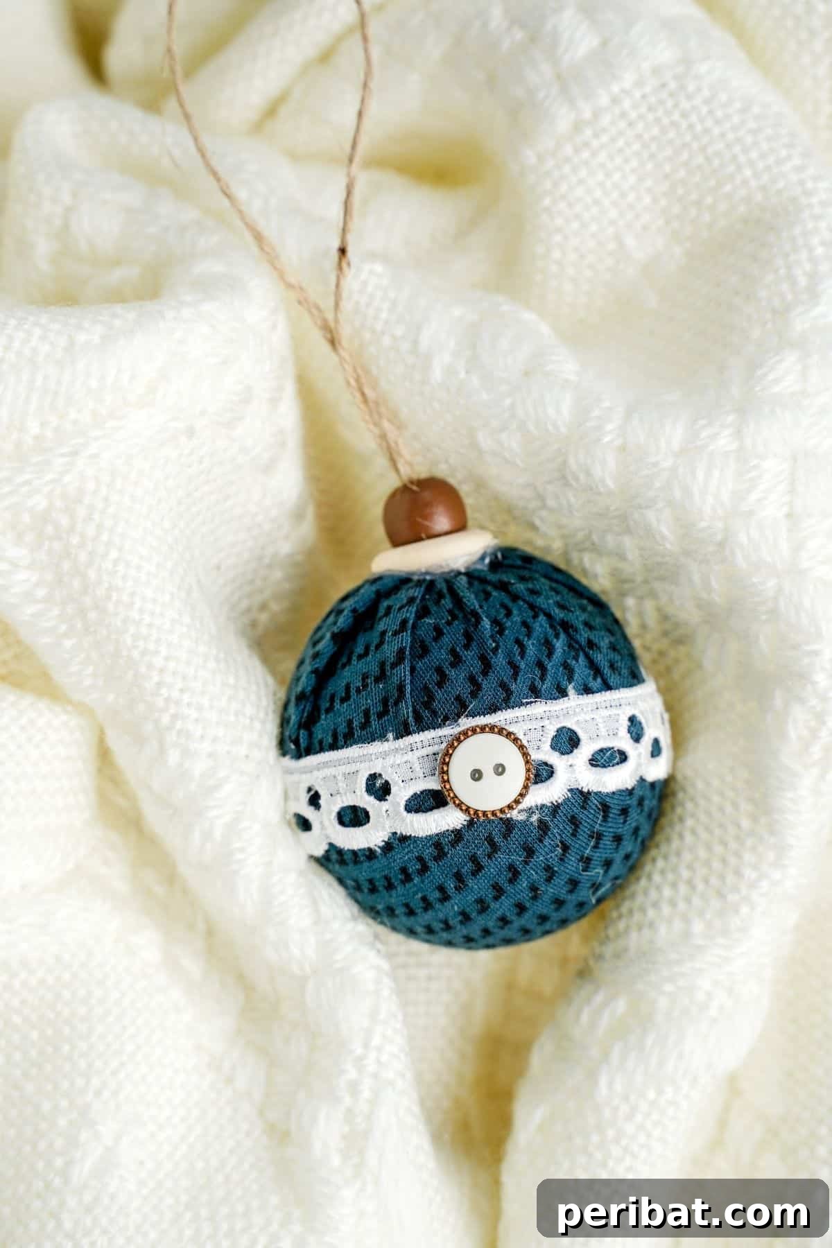 Chic Fabric Holiday Bauble 16 A green fabric ornament resting on a soft white blanket, highlighting its texture and design