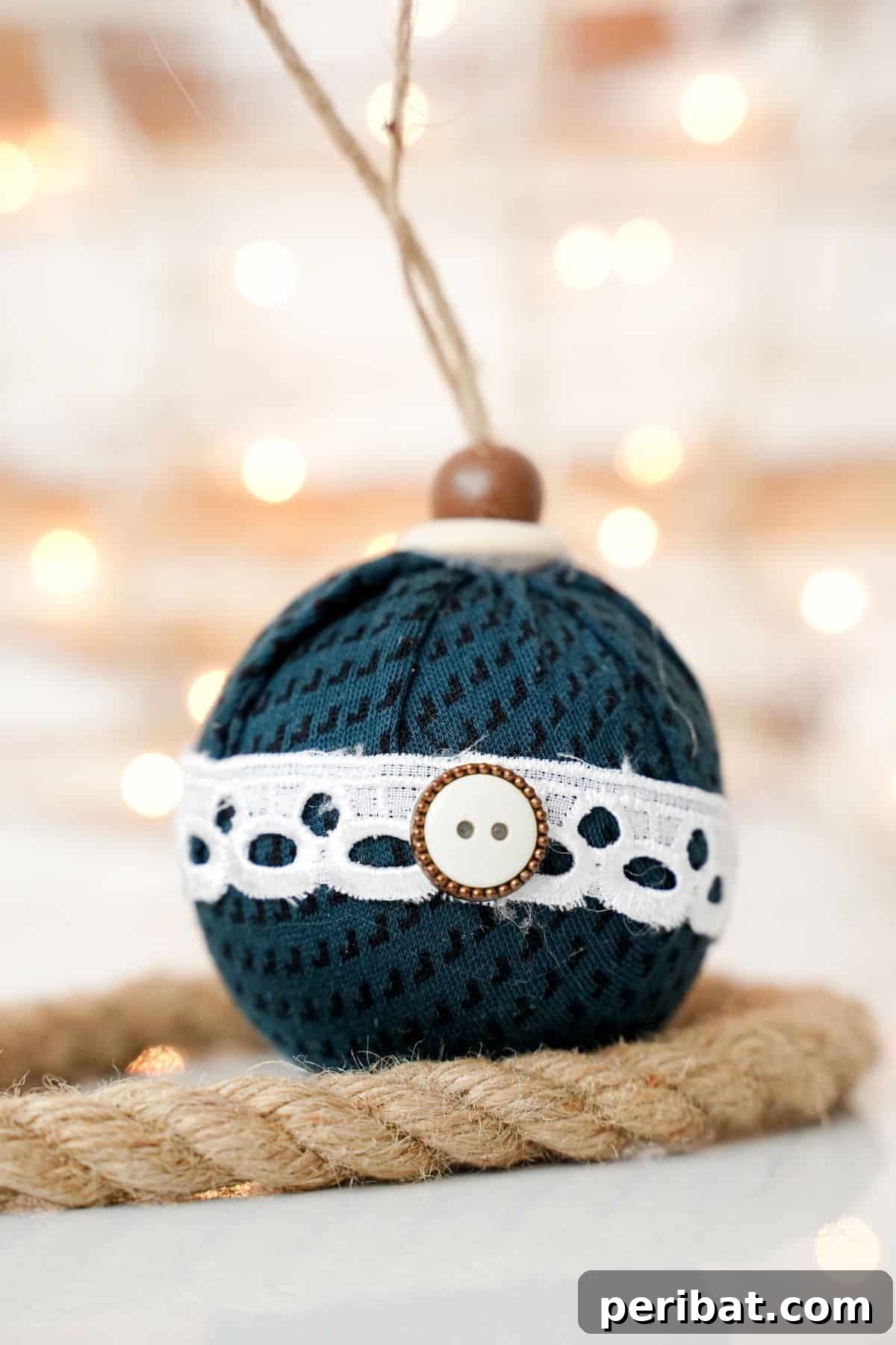 Chic Fabric Holiday Bauble 18 Close-up of a fabric ball ornament on a wooden table, with twine detail and blurred lights in the background