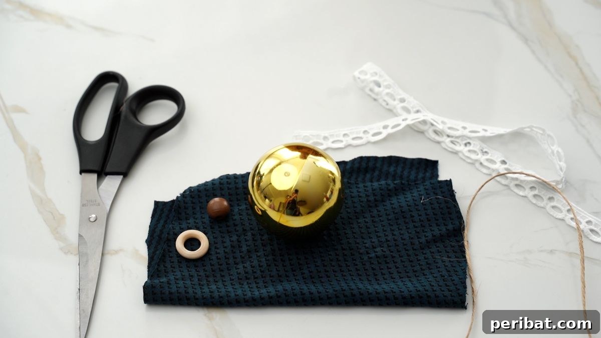 Chic Fabric Holiday Bauble 4 Gold Christmas ornament on soft green fabric, surrounded by lace, scissors, and a hot glue gun on a marble table