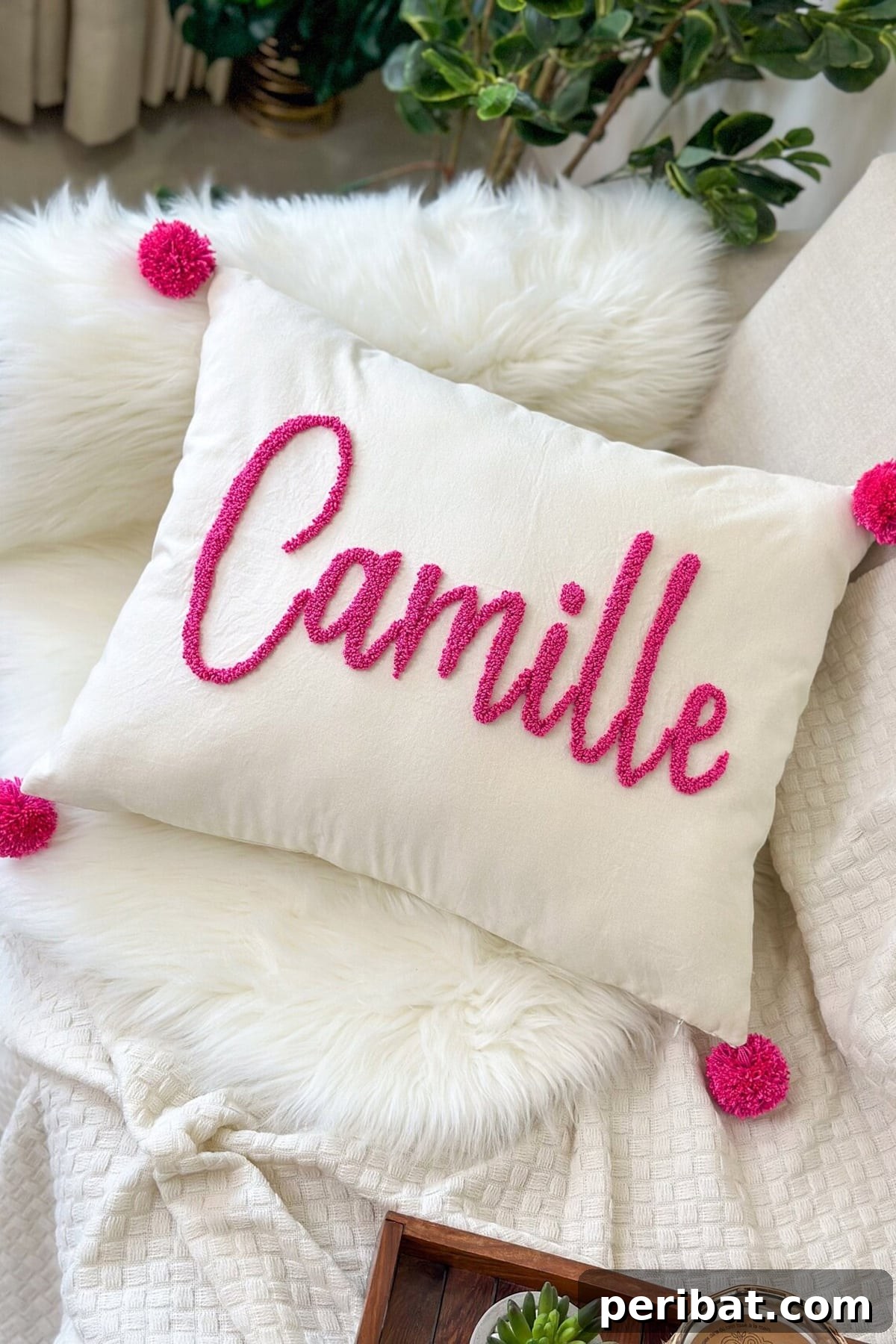 A decorative pillow cover created with punch needle embroidery and enhanced with fluffy pom pom borders.