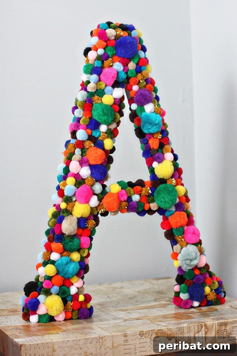 A decorative monogram letter 'E' artfully covered with an assortment of small, multicolored pom poms.