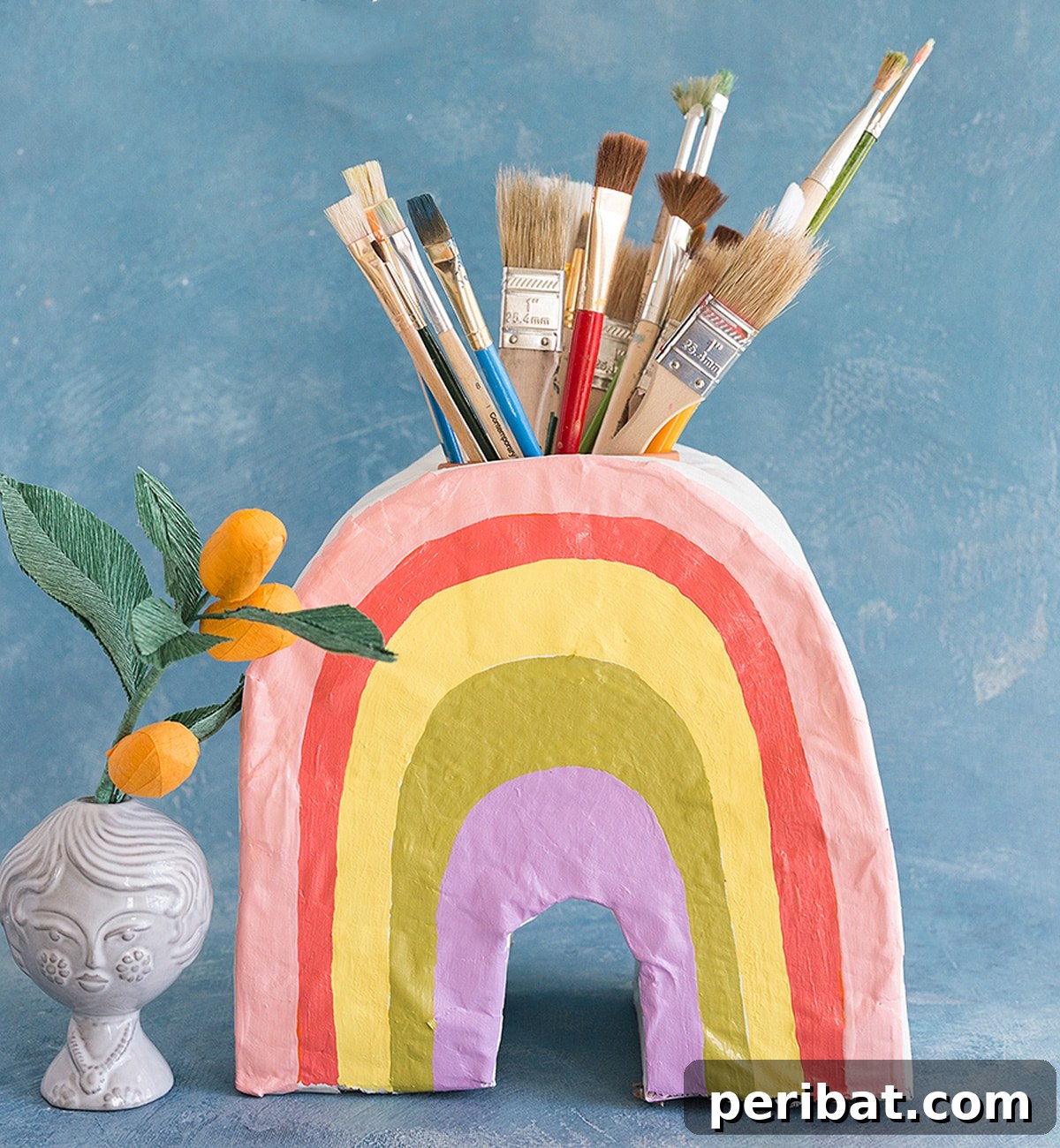 Vibrant paper mache rainbow vase filled with colorful craft supplies