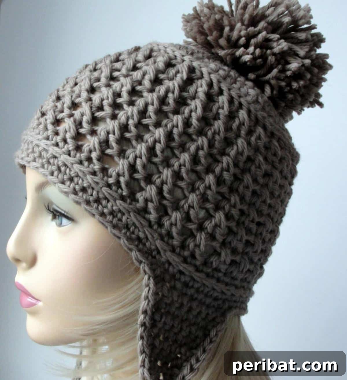 32 Cozy Ear Flap Hat Knitting Designs 34 A stylish ear flap hat created with a crochet pattern, featuring bulky weight yarn and a fluffy pompom.