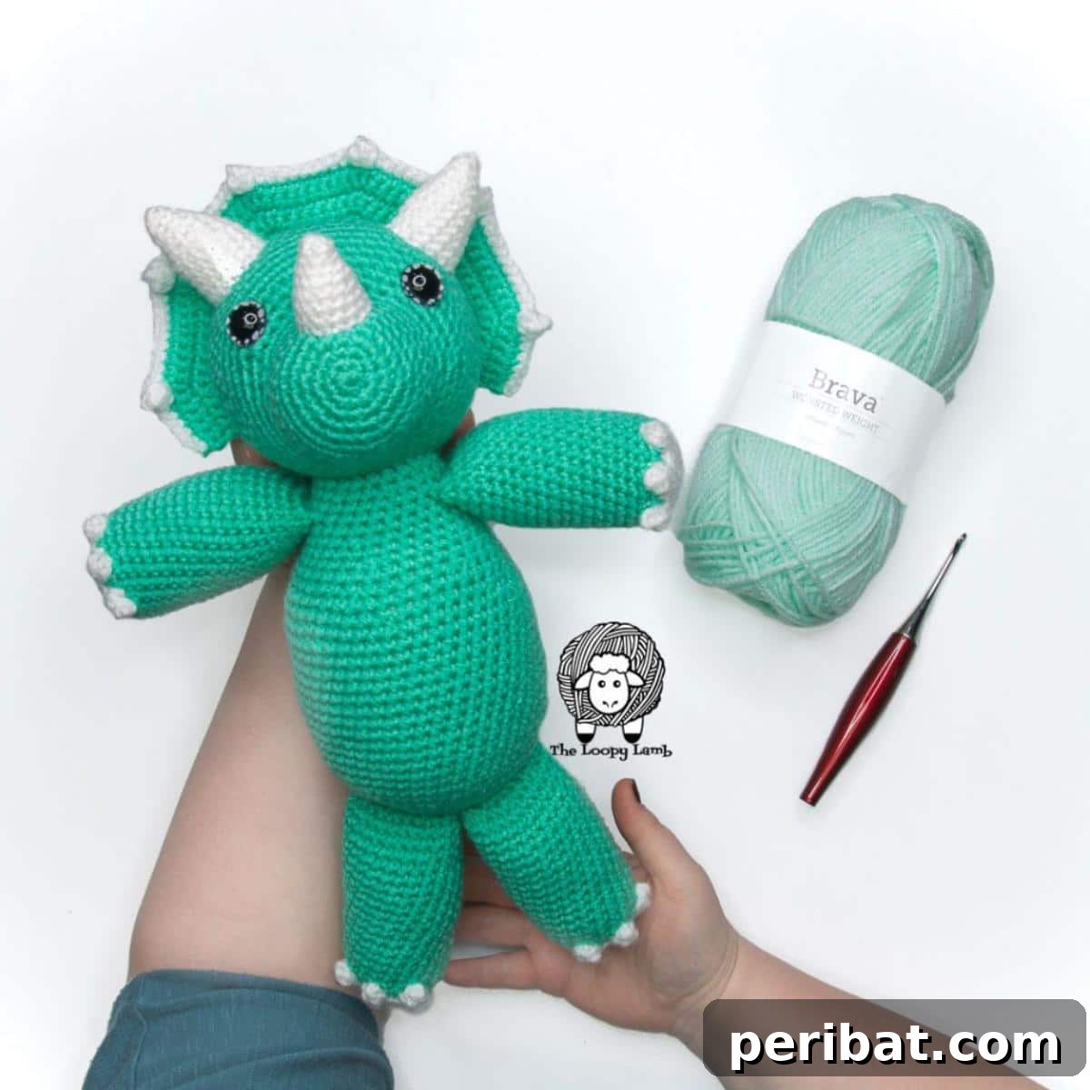 A charming green amigurumi Triceratops crochet toy with distinctive horns and a frill.