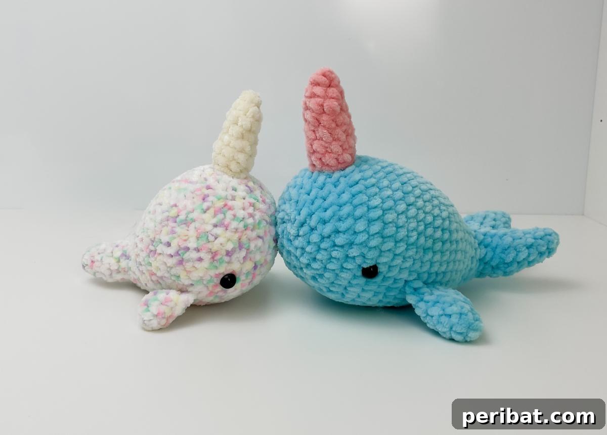 A pair of cute amigurumi crochet narwhals, one in blue and one in pink, with their distinctive horns.
