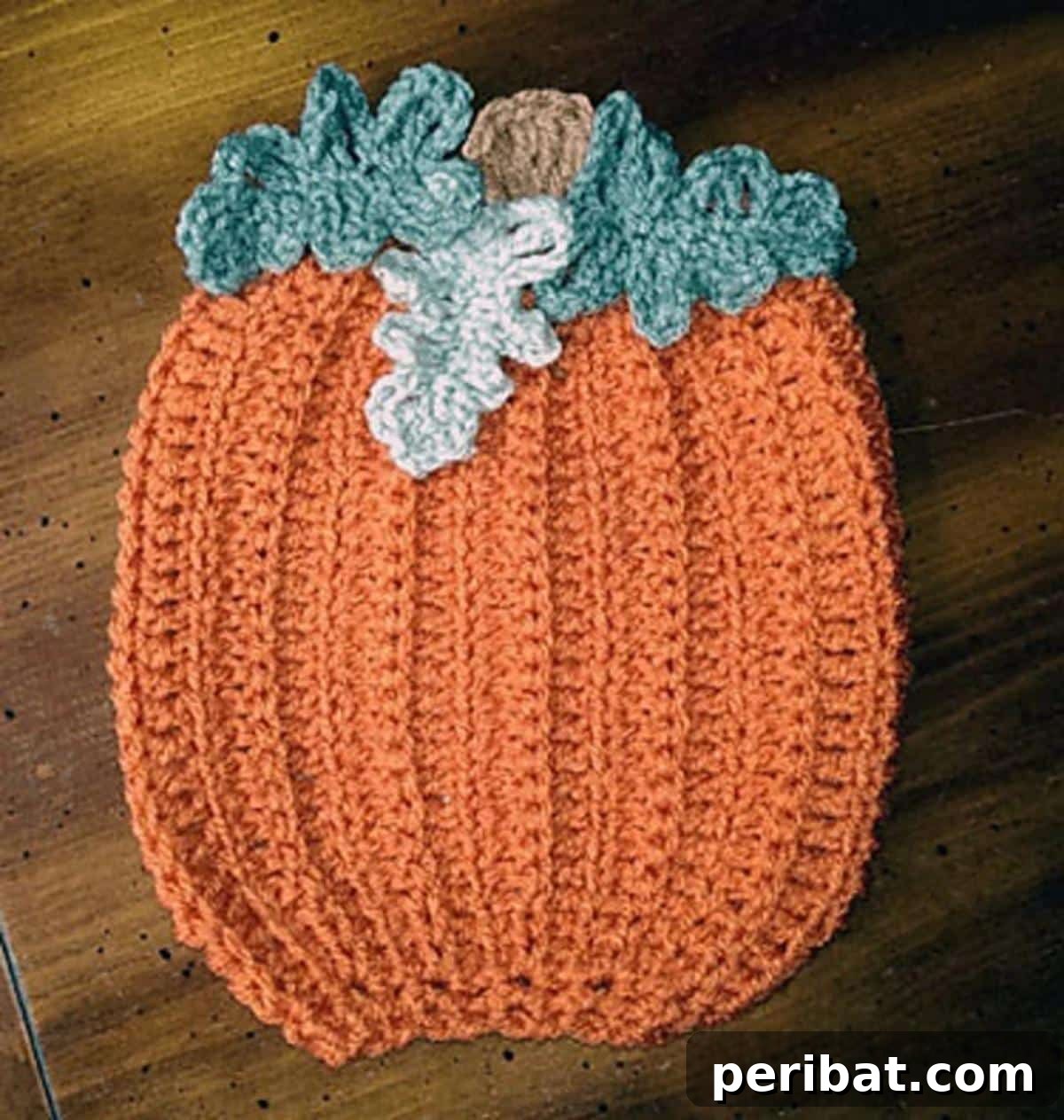 An autumnal pumpkin patch decorative crochet potholder, featuring a prominent orange pumpkin motif and subtle green leaf details.