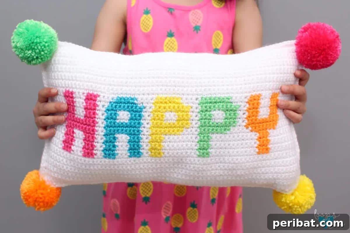 40 Creative Crochet Pillow Projects 22 A cheerful 'Happy' crochet pillow, featuring vibrant rainbow stripes and playful pompoms, with bold block letters spelling 'Happy'.
