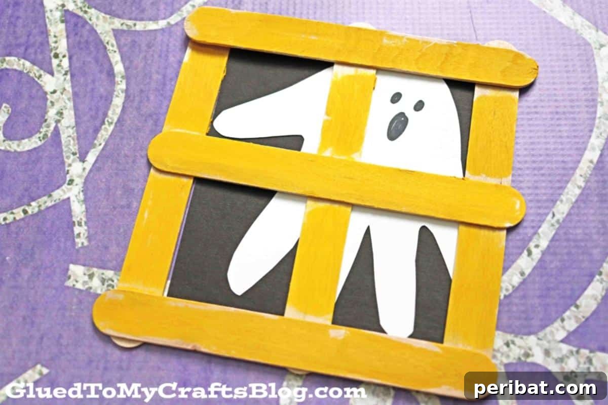 Spooktacular Popsicle Stick Halloween Projects 11 A cute ghost figure made from popsicle sticks, painted white with googly eyes, designed to be hung in a window.