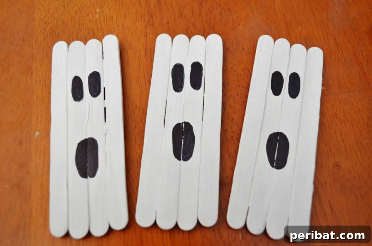Spooktacular Popsicle Stick Halloween Projects 21 A group of white-painted popsicle stick ghosts with black eyes, arranged as part of a Halloween craft display for kids.