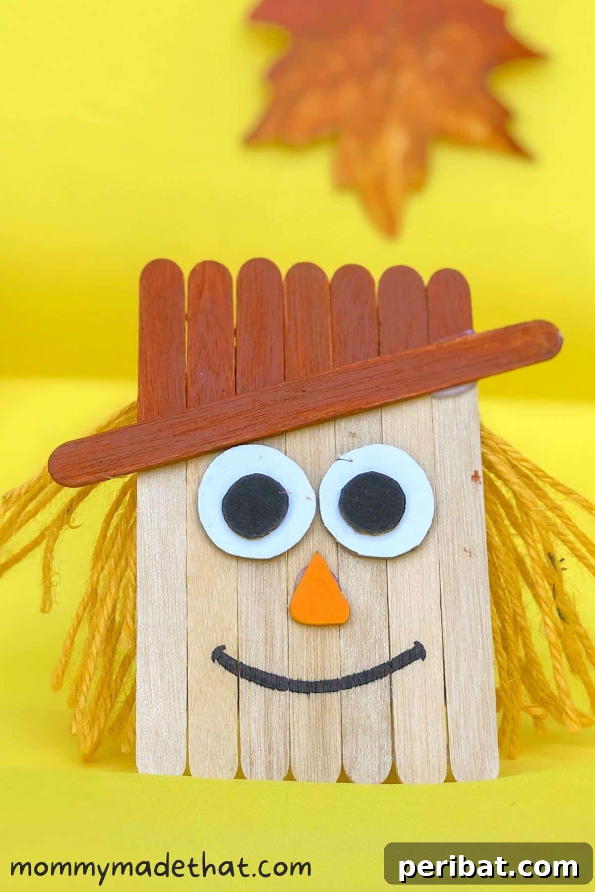 Spooktacular Popsicle Stick Halloween Projects 23 A charming scarecrow craft made from popsicle sticks, adorned with a checkered hat and fabric details, perfect for autumn decorations.