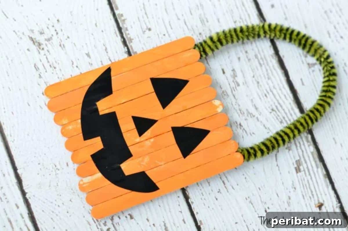 Spooktacular Popsicle Stick Halloween Projects 7 A festive Halloween pumpkin door hanger crafted from popsicle sticks, painted orange with a green stem and a friendly jack-o'-lantern face.