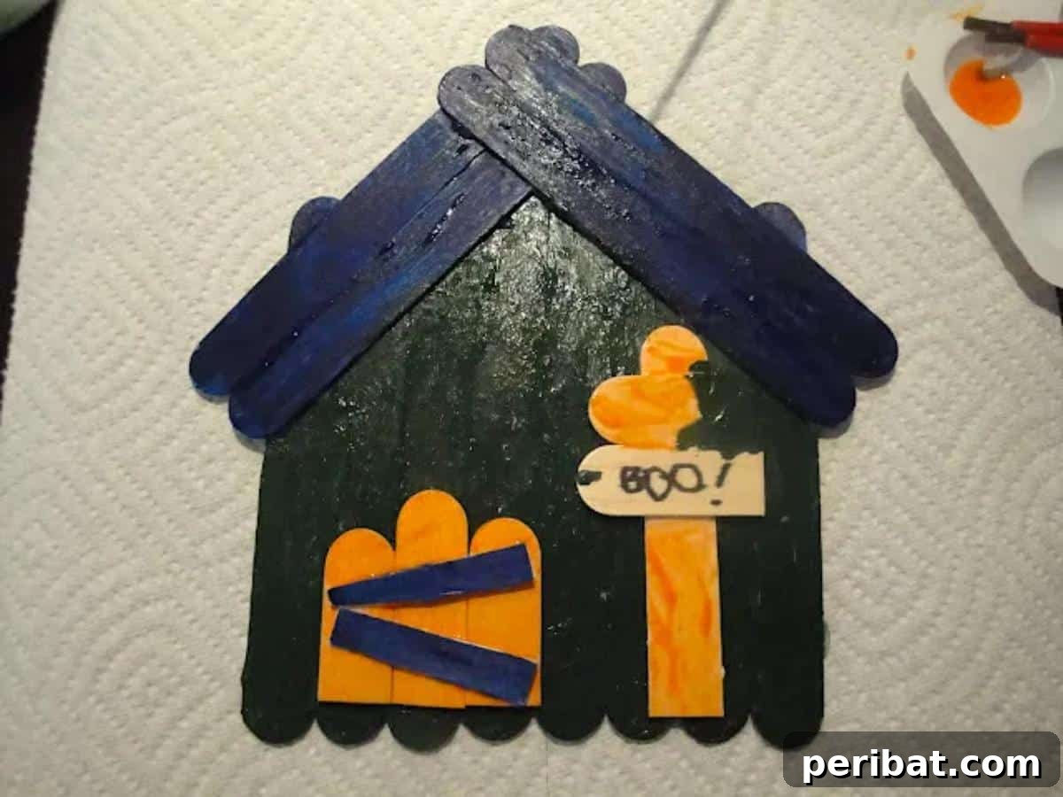 Spooktacular Popsicle Stick Halloween Projects 8 A miniature haunted house made from popsicle sticks, painted in dark colors with spooky details like windows and a roof.