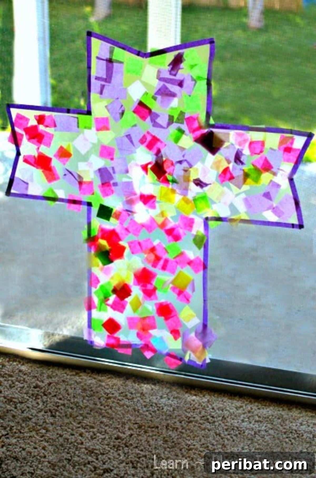 A colorful cross suncatcher made with tissue paper glowing in sunlight.