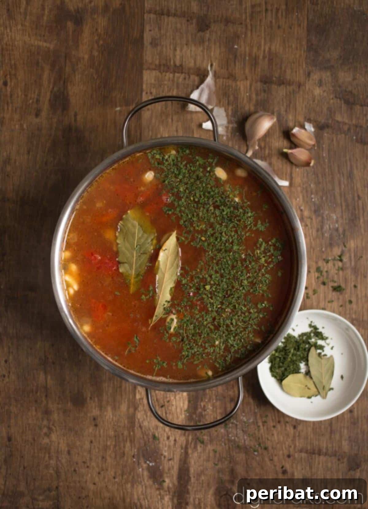 Hearty White Bean and Crispy Bacon Soup: Your Winter Blues Remedy 6 Dried parsley flakes and bay leaves being added to the soup, enhancing its aroma and flavor.