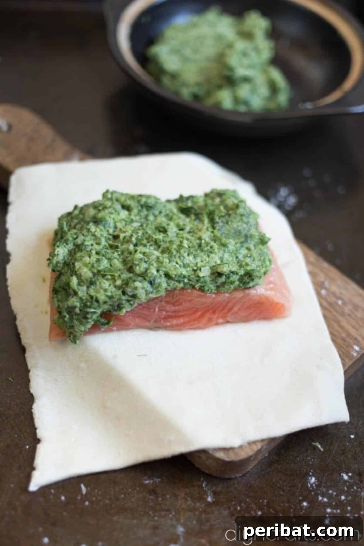 Elevate Your Brunch: Light Salmon Wellington Perfection 5 A salmon fillet being generously coated with the spinach and parmesan cheese filling on a cutting board.