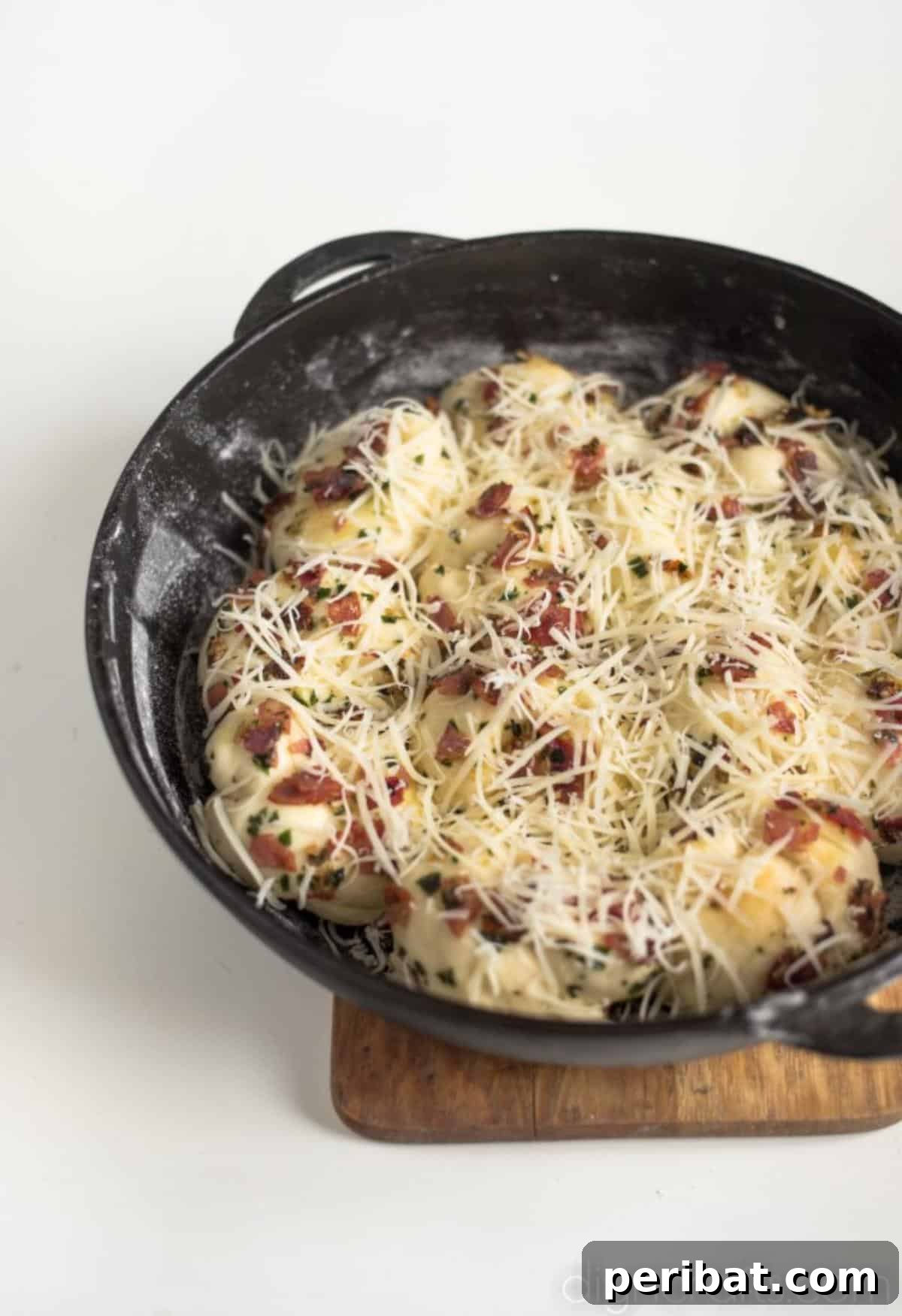Pull-Apart Pepperoni Garlic Knots: Pure Appetizer Perfection 6 Pepperoni garlic knots arranged in a cast iron skillet, covered with grated cheese, before baking.
