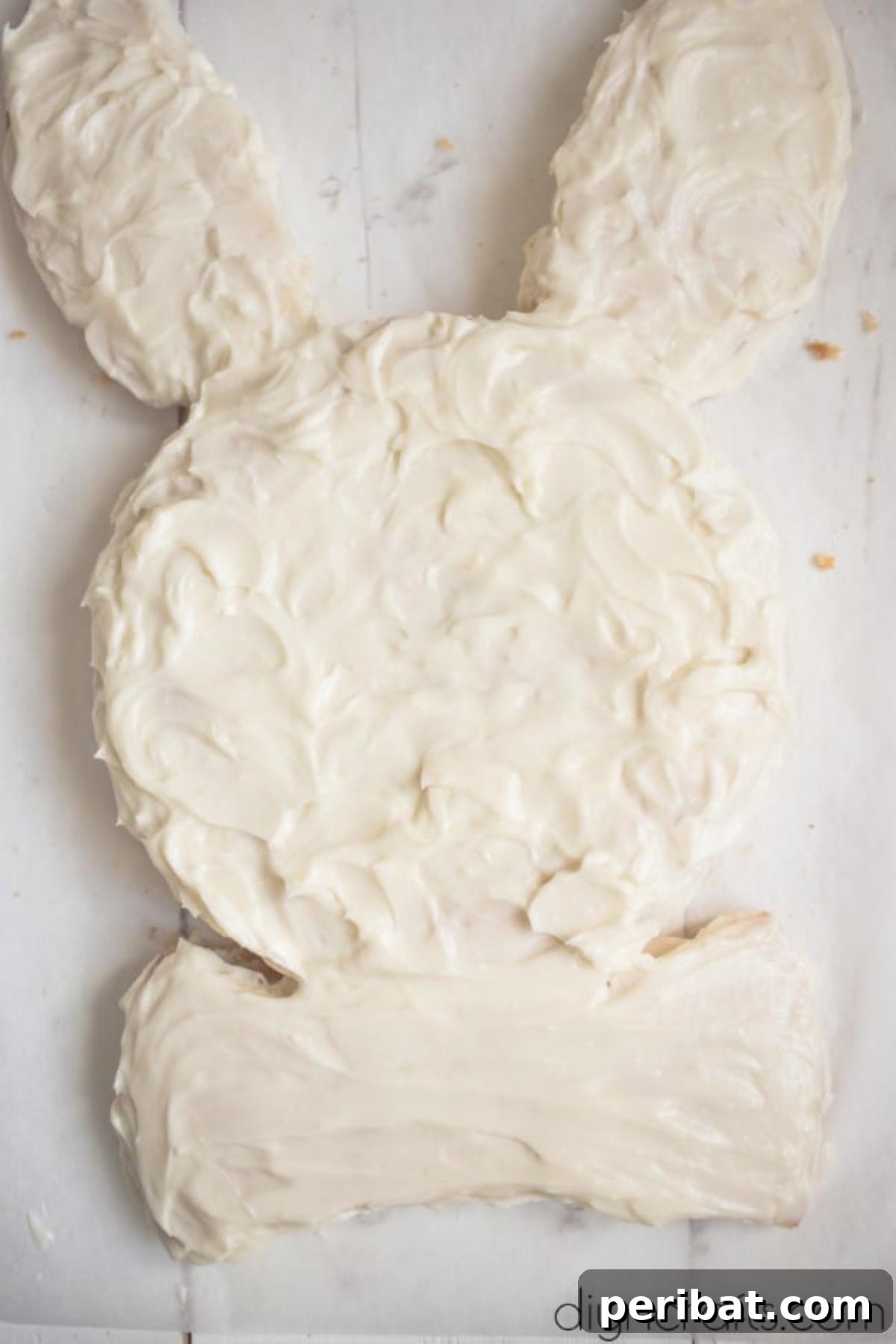 Hem Şirin Hem Lezzetli Paskalya Tavşanı Pastası Tarifi 8 The Easter Bunny cake fully covered with a smooth layer of cream cheese frosting. The entire surface is coated, providing a perfect canvas for further decoration and bringing the bunny form to life.