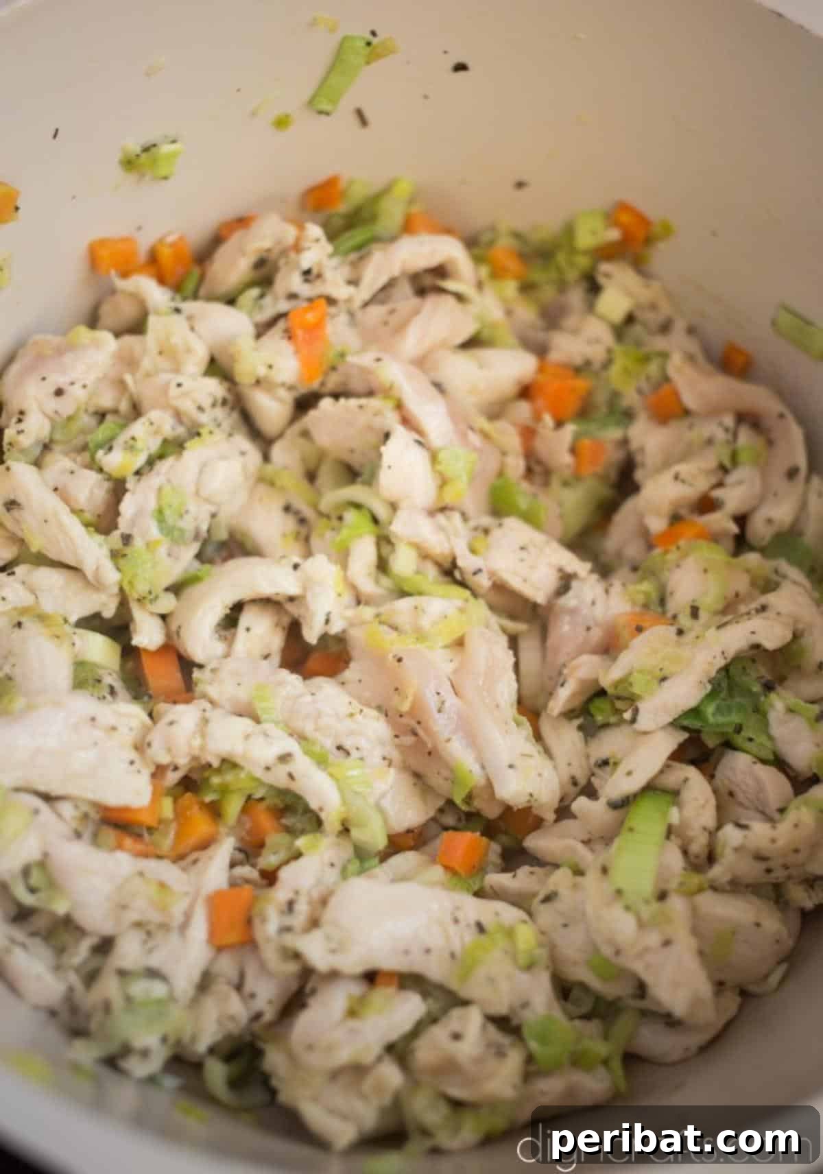 Close-up of chicken breast, leeks, carrots, and herbs sautéing in a pan.