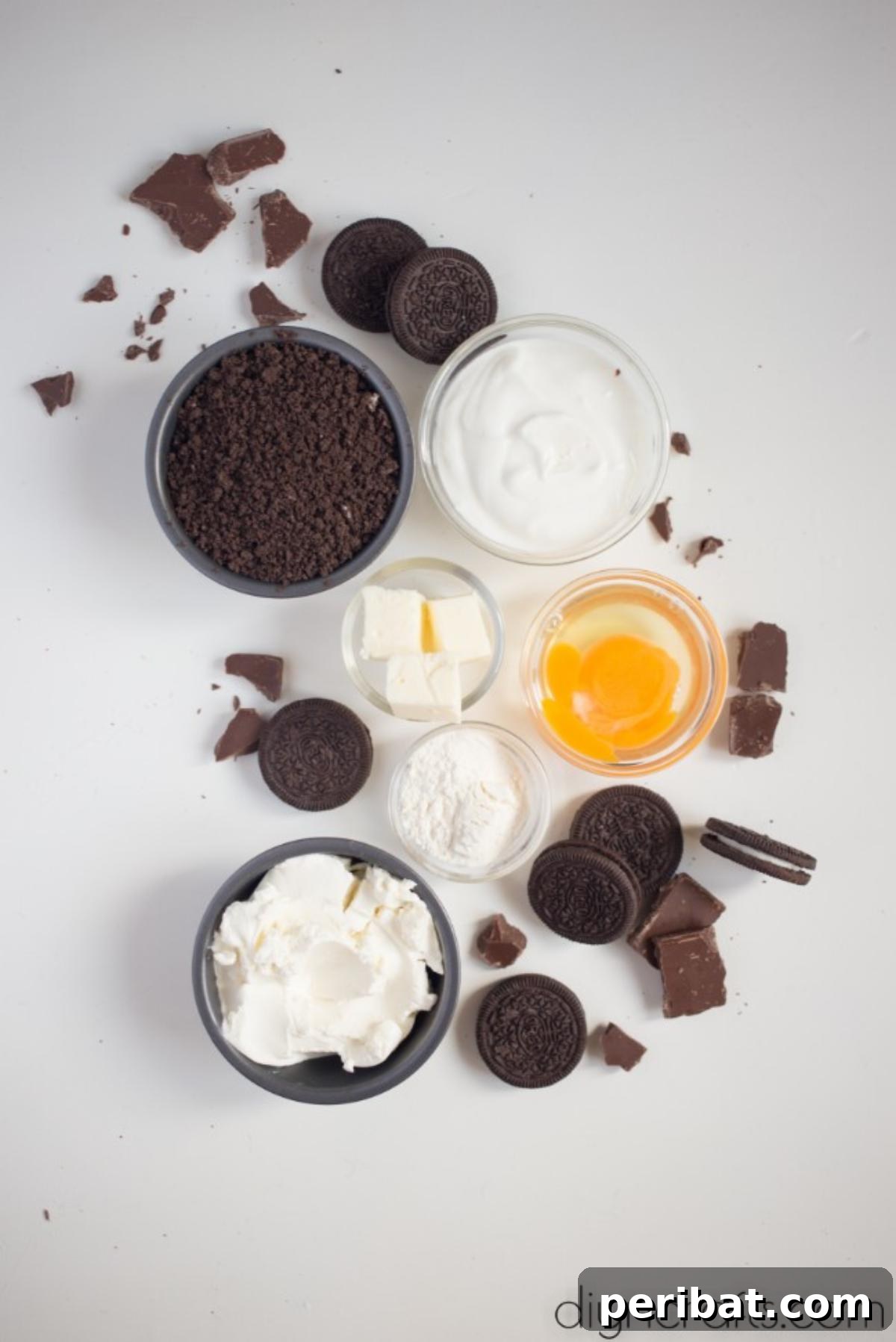 Ingredients for Oreo Cheesecake Bites - A flat lay showcasing the key ingredients: a package of cream cheese, a carton of sour cream, a bag of flour, a stick of butter, a bowl of crumbled Oreos, and whole Oreos on a wooden surface.