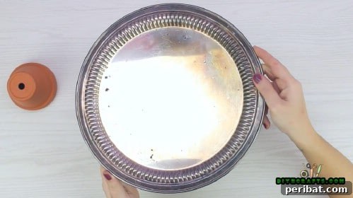 The larger silver tray carefully placed and glued onto the base of the inverted large clay pot, forming the first tier.