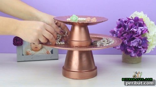 The completed two-tiered jewelry stand after being spray-painted a shimmering gold color, ready for use.
