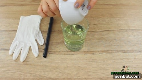 Dish soap being added to the glycerin and water mixture, with a spoon nearby for gentle stirring.