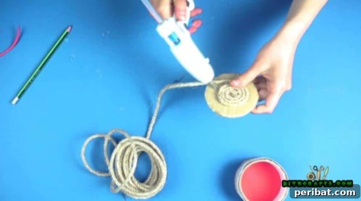 Applying twine in a spiral pattern to cover the second cardboard circle, forming the lid.
