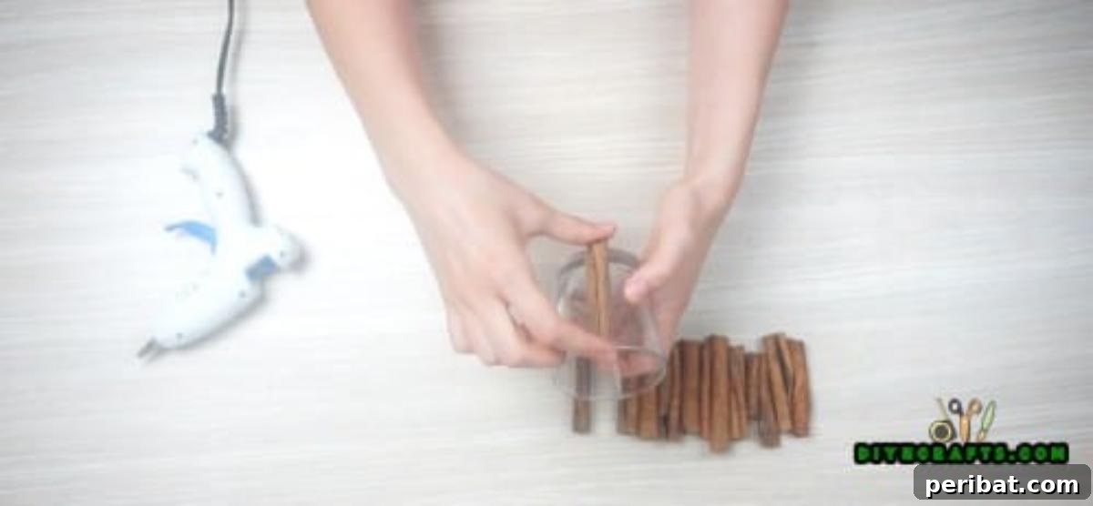 DIY Beautiful Candle Holders From Simple Materials 3 Applying hot glue to a cinnamon stick to attach it to a clear glass votive holder, starting the rustic candle holder project.