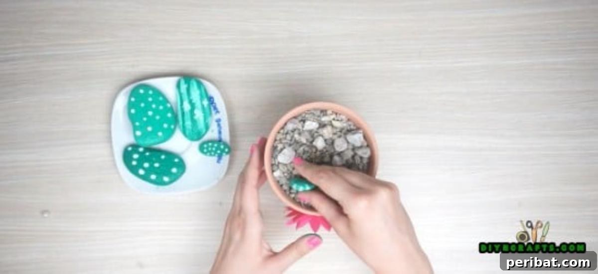 Inserting painted stone cacti into a small flower pot filled with gravel.