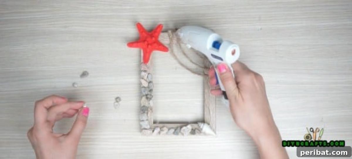 Applying small garden gravel and shells to a wooden picture frame with hot glue.