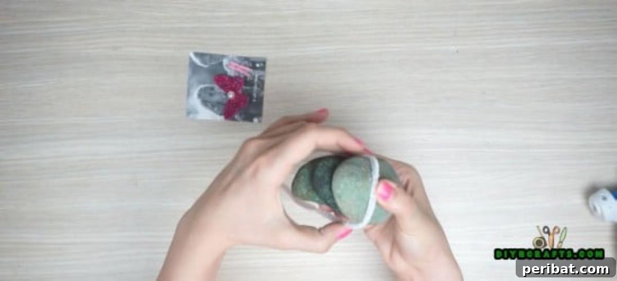 Wrapping a pipe cleaner around the glued river stones for added decoration and stability.