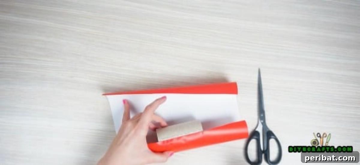 Wrapping decorative paper around a toilet paper roll for a DIY paper roll candy craft.