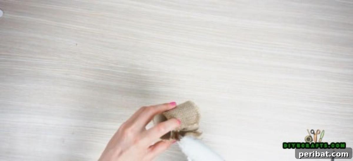Gluing burlap around a small paper roll segment to create the base of a DIY napkin ring.