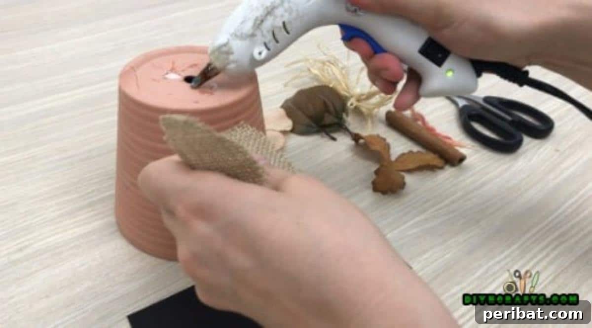 Applying hot glue to the inverted ceramic flower pot base for the jack-o-lantern stem