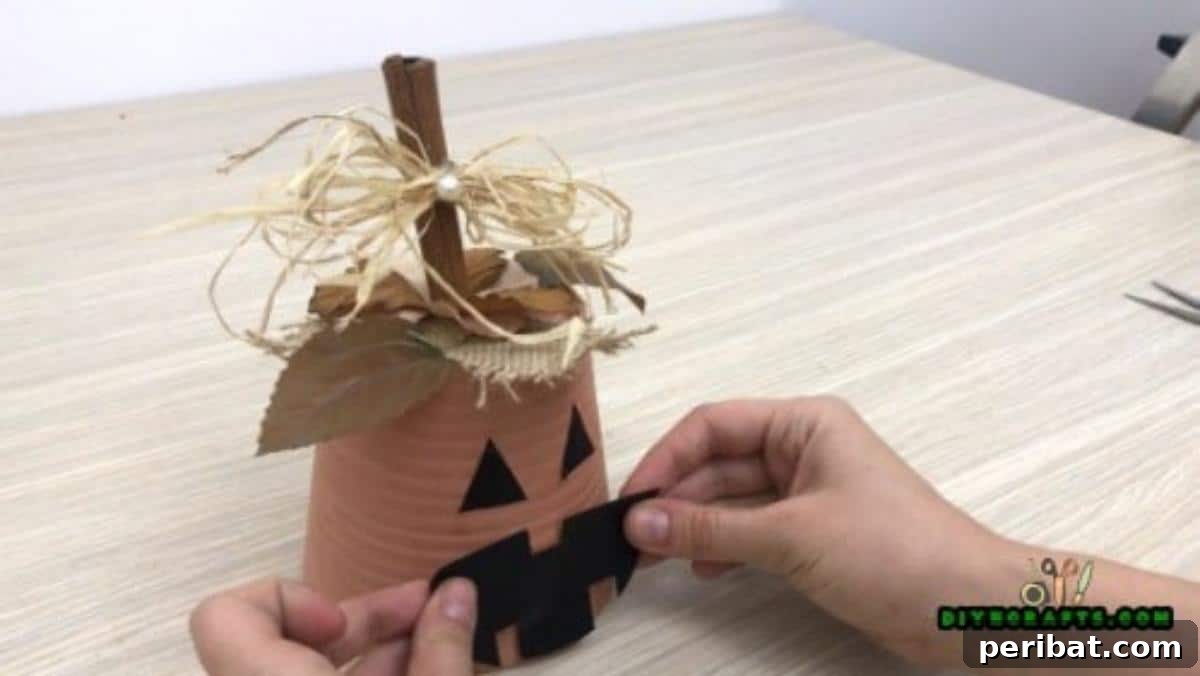 Attaching the black paper mouth shape to complete the flower pot jack-o-lantern's expression