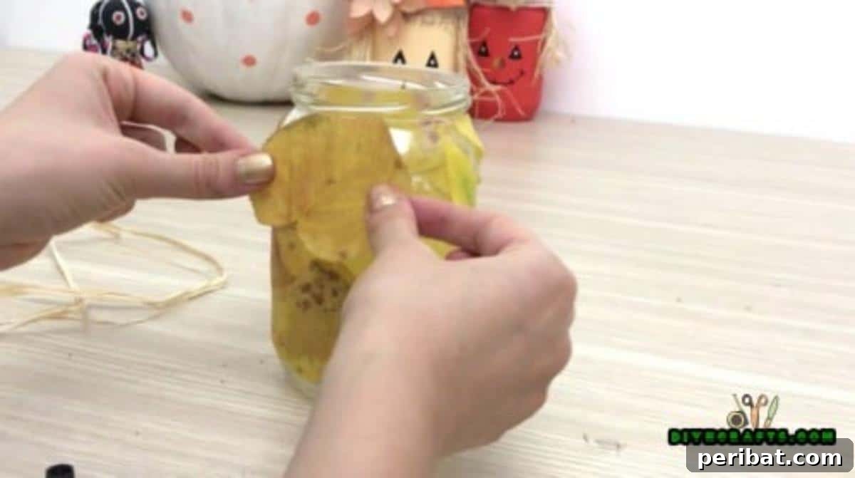 Minutes to Marvelous: 5 Easy Fall DIY Decor Projects 15 Continued process of gluing vibrant autumn leaves onto the glass jar, building up a full, colorful covering for the DIY lamp.